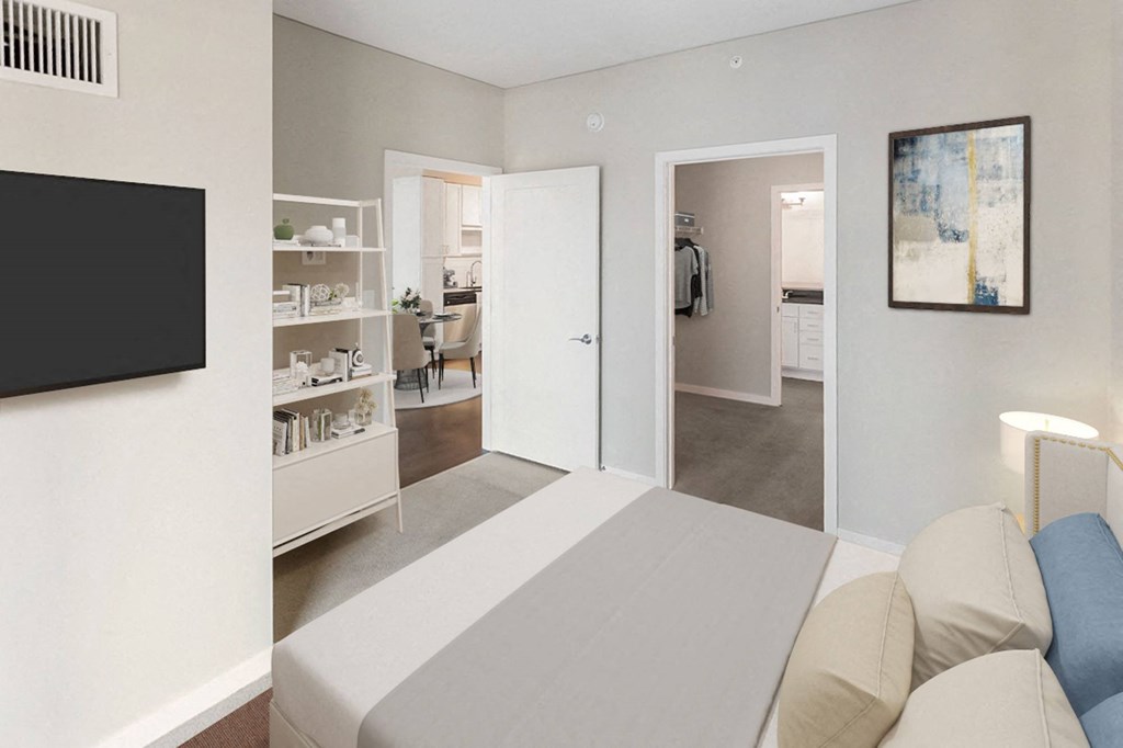Modern bedroom here at Nic on 5th Apartment Homes featuring a neatly made bed with beige and blue pillows, a wall-mounted TV, a white shelf adorned with decor, open doors leading to a dining area and closet. Neutral tones and minimalistic art create a calm, inviting atmosphere.
