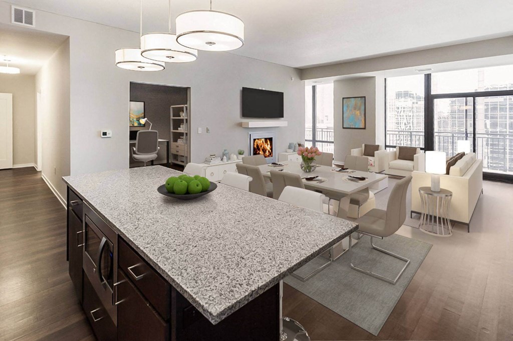 Modern open-concept living area here at Nic on 5th Apartment Homes with a stone kitchen island, green apples, elegant dining table, cozy fireplace, and large windows with city views.