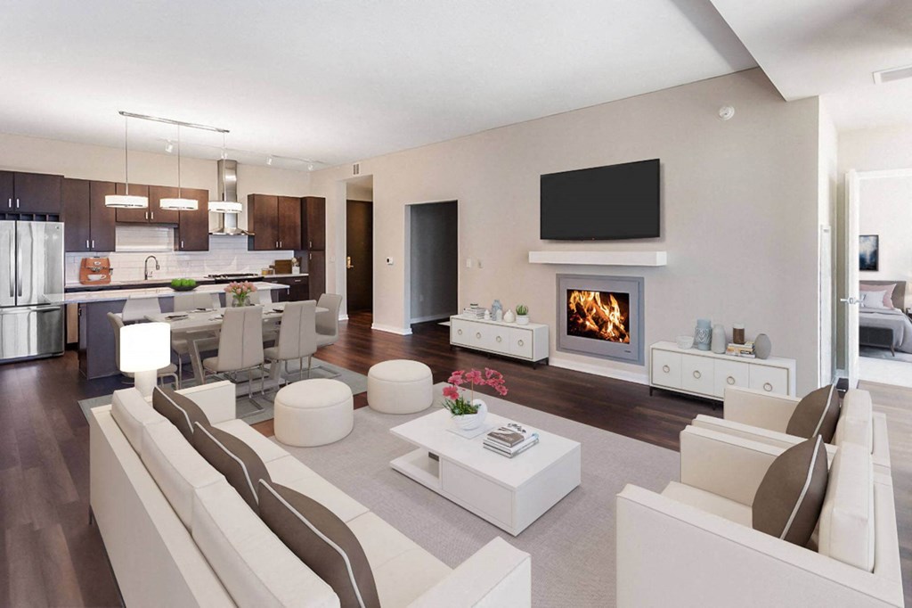 Modern open-plan living space with a kitchen, dining, and living area here at Nic on 5th Apartment Homes. Features dark wood floors, white furniture, a cozy fireplace, and a wall-mounted TV.
