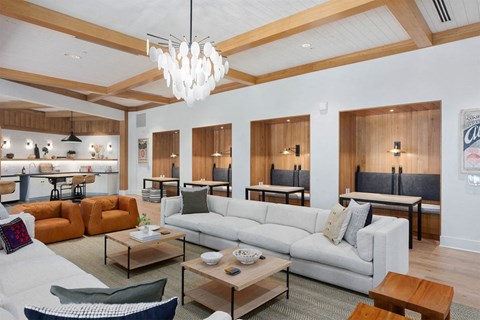 Modern resident lounge here at Reflect at Dobson Ranch Apartments with cozy seating, light wood accents, and a sleek chandelier. Features leather chairs, white sectional, and wood dining booths, creating a warm, inviting atmosphere.