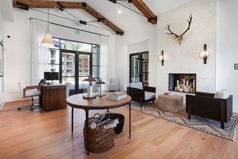 Modern living room here at Reflect at Dobson Ranch Apartments with wood beams, a large round table, baskets underneath, and armchairs by a white stone fireplace adorned with deer antlers.