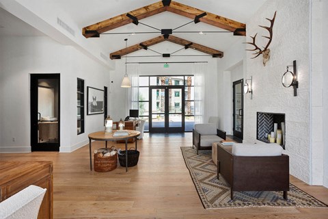 Modern living room here at Reflect at Dobson Ranch Apartments with high wooden beam ceiling, antler decor, and cozy fireplace. Natural light through glass doors creates a warm, inviting atmosphere.