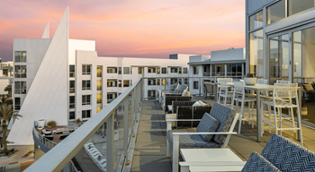 a communal terrace with tables and chairs and a sunset over a building