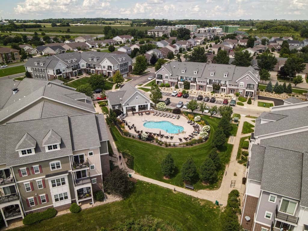 Aerial view of a Glacier Valley Apartment community with townhouses and apartments. Central swimming pool surrounded by loungers, greenery, and parked cars.