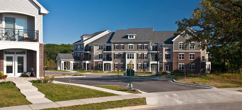 Modern Glacier Valley apartment complex with gray and red brick buildings under a clear blue sky. Manicured lawns and sidewalks give a peaceful, suburban feel.