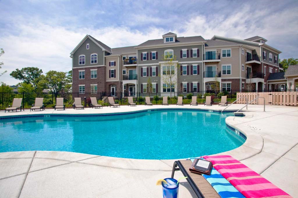 Glacier Valley Apartment complex with a serene outdoor pool. Poolside chairs line the perimeter, and a colorful towel rests on a chair, conveying a relaxing atmosphere.
