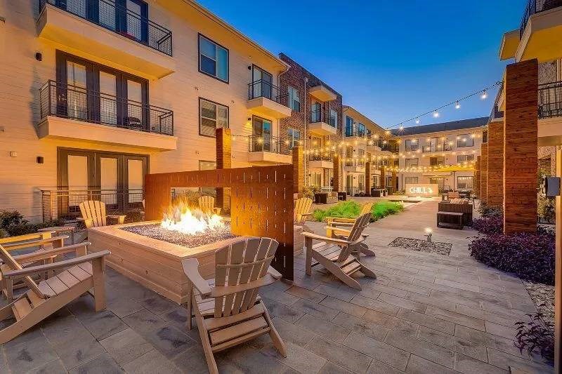 Cozy courtyard of Skyline at Farmers Market Apartment Homes at dusk, featuring a glowing fire pit surrounded by wooden chairs, string lights above, and balconies.
