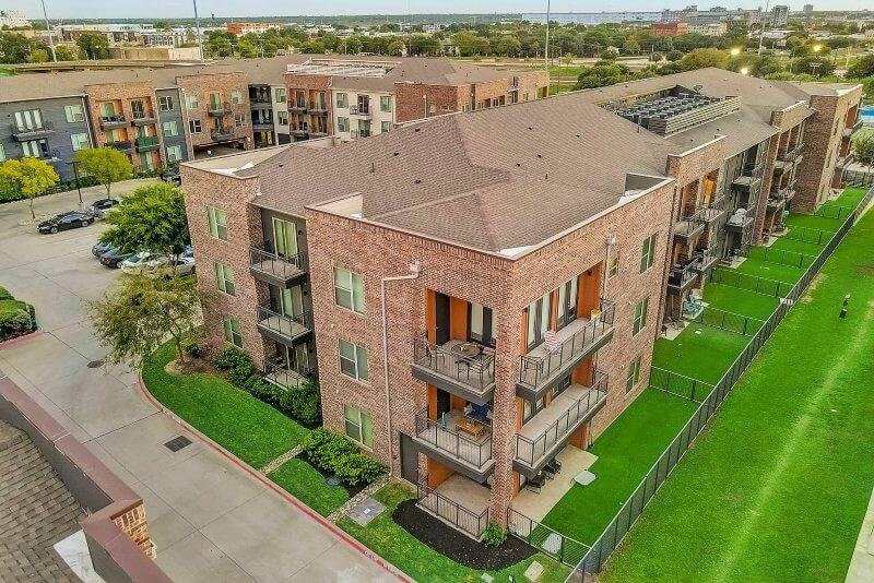 Aerial view of Skyline at Farmers Market Apartment Homes with balconies, surrounded by greenery and a neatly maintained parking area, under a clear sky.