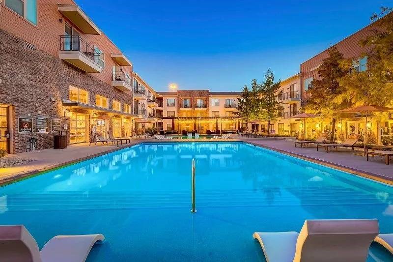 Luxurious Skyline at Farmers Market Apartment Homes at dusk with a glowing outdoor pool surrounded by lounge chairs and trees, creating a serene and inviting ambiance.
