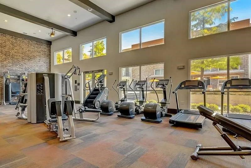 Bright, modern gym here at Skyline at Farmers Market Apartment Homes with treadmills, ellipticals, and weight machines. Large windows let in natural light, creating an energetic and inviting atmosphere.