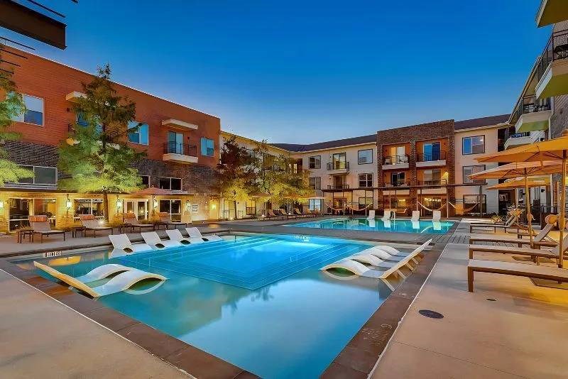 Modern Skyline at Farmers Market Apartment Homes at dusk with a lit swimming pool, surrounded by lounge chairs and shaded seating, creating a relaxing, inviting ambiance.