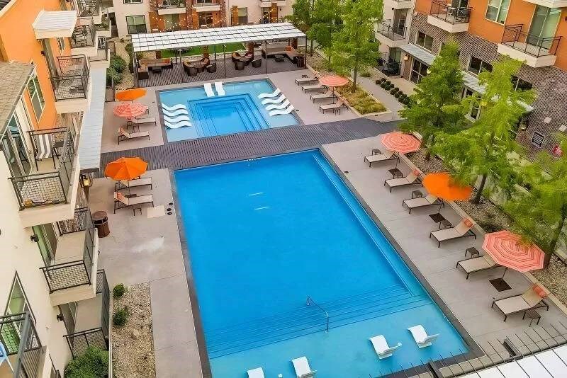 Aerial view of Skyline at Farmers Market Apartment Homes with two pools. Surrounding the pools are sun loungers and orange umbrellas, creating a relaxed, inviting atmosphere.