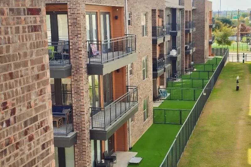 Modern Skyline at Farmers Market Apartment Homes with brick exterior, multiple balconies, and green artificial turf yards. The scene is calm, with clear views of suburban surroundings.