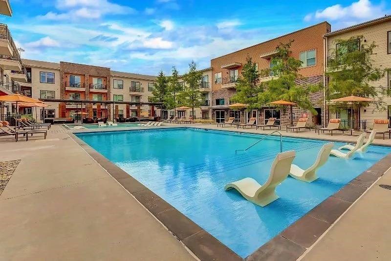 Modern courtyard here at Skyline at Farmers Market Apartment Homes with a rectangular pool, surrounded by lounge chairs and umbrellas. Clear blue sky above, creating a calm, inviting atmosphere.