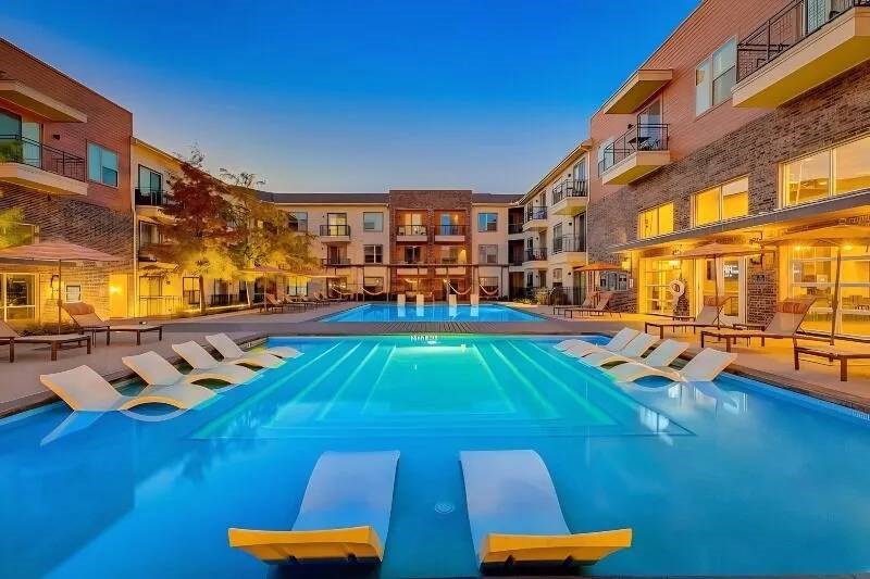 Modern Skyline at Farmers Market Apartment Homes at dusk with illuminated windows, surrounding a central swimming pool. Lounge chairs and warm lighting create a serene, inviting atmosphere.