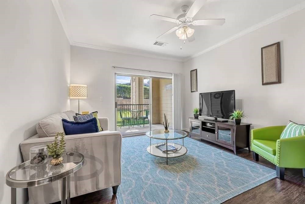 A living room with a grey couch, a green chair, a glass coffee table, and a television.