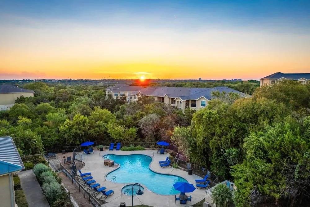 A sunset view of a pool area with lounge chairs and trees.