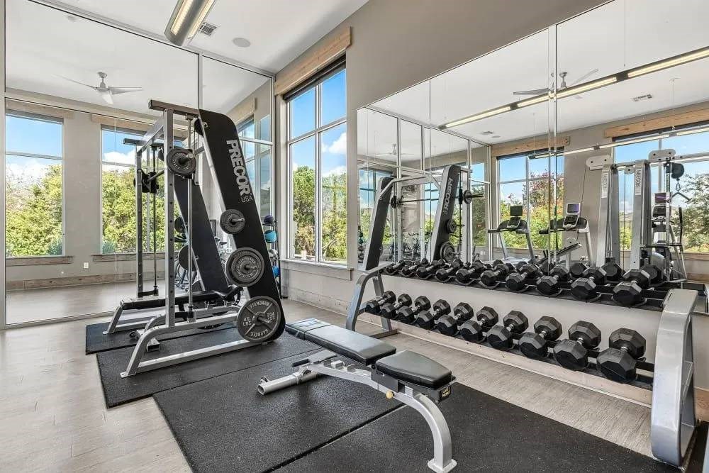 A gym with a variety of equipment including a leg press machine, a bench press, and dumbbells.