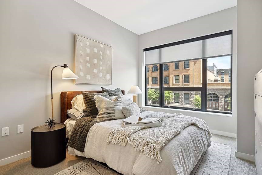 A bedroom with a large bed and a large window overlooking a city.