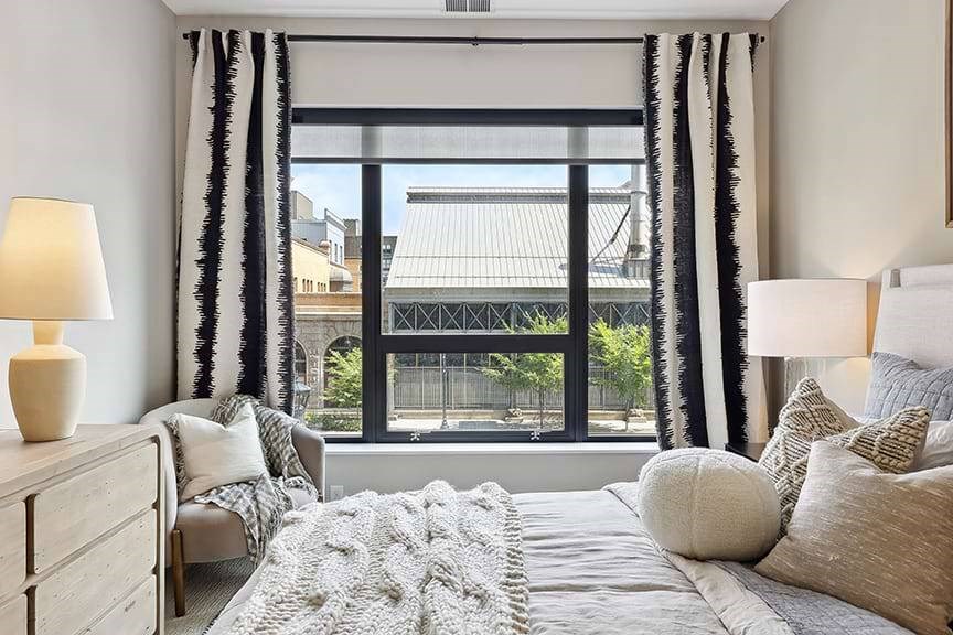 A bedroom with a large bed, a chair, and a window with a view of the city.