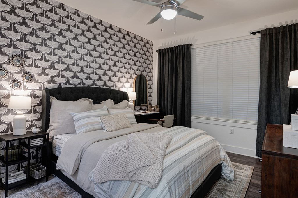 Bedroom at The Reserve at Arboretum Apartment Homes with a modern design, featuring a geometric black and white accent wall, cozy bed with striped bedding, dark curtains, and soft lighting.