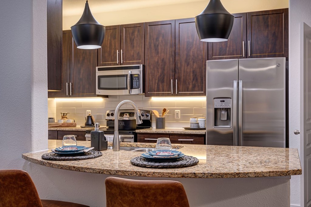 Modern kitchen here at The Reserve at Arboretum Apartment Homes with wooden cabinets and stainless steel appliances, like a fridge and microwave. A granite island features elegant table settings.