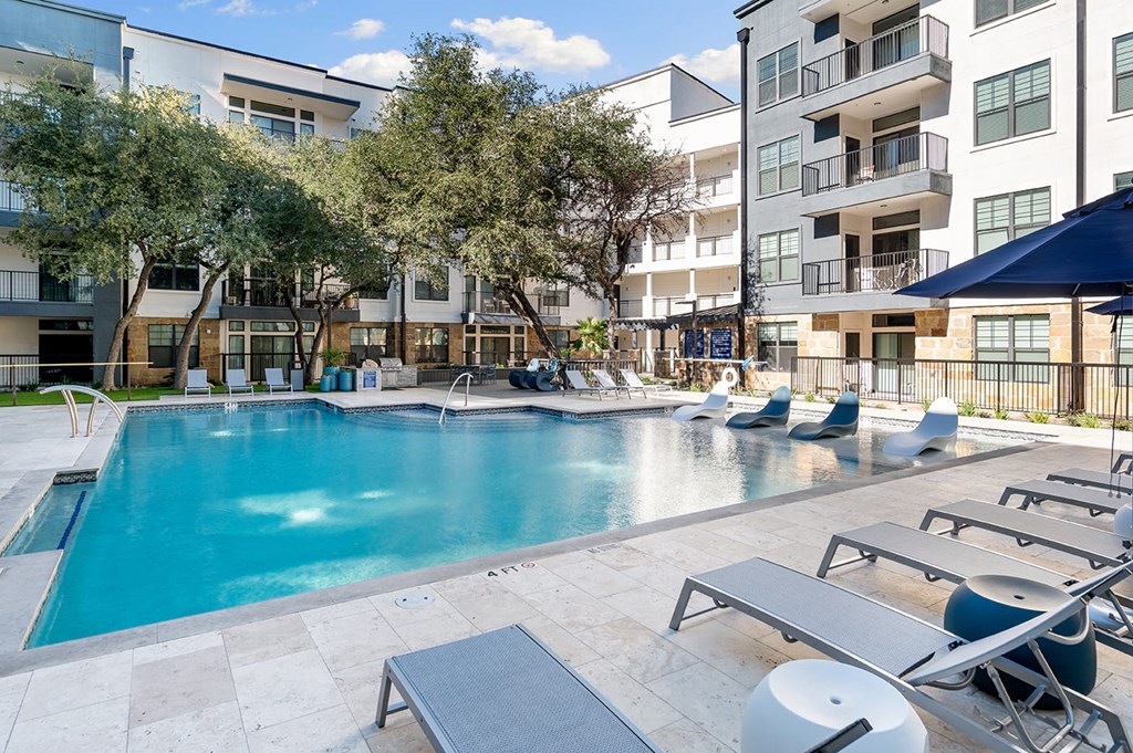 Modern courtyard here at The Reserve at Arboretum Apartment Homes with a large outdoor pool surrounded by lounge chairs and umbrellas. Trees provide shade, creating a relaxed atmosphere.