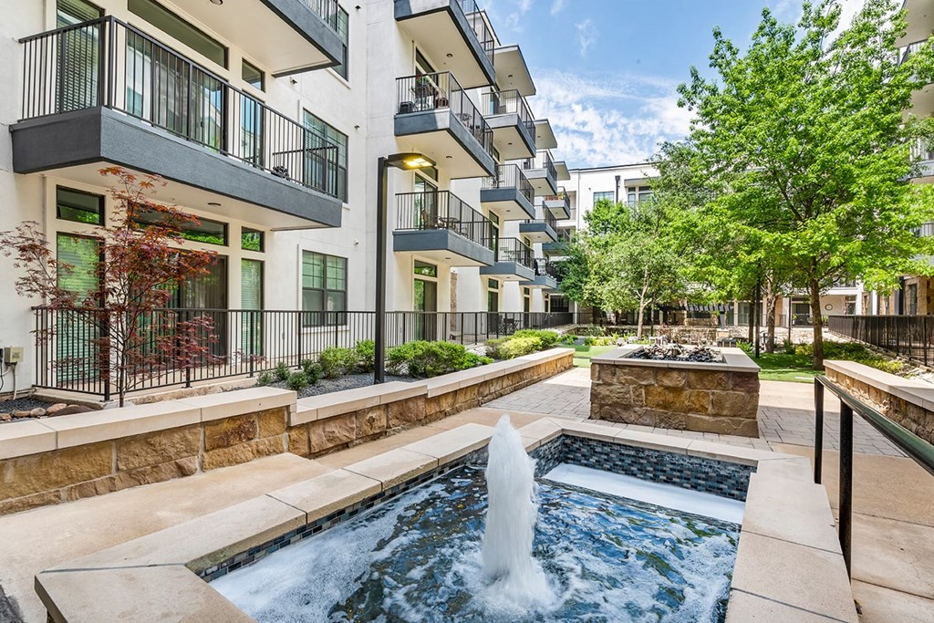 Modern courtyard here at The Reserve at Arboretum Apartment Homes with a central fountain, surrounded by greenery and trees. Balconies overlook the serene, clean, and inviting space.