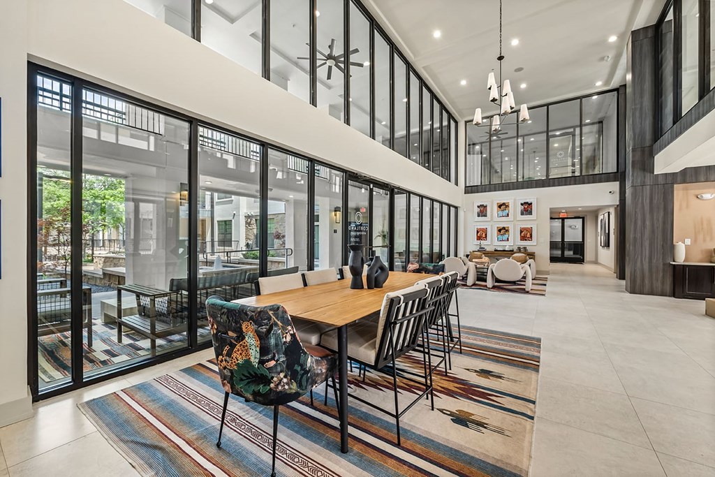 Spacious, modern lobby here at The Reserve at Arboretum Apartment Homes with high ceilings and large windows. Features a wooden table, patterned chairs, and colorful rugs, creating a welcoming ambiance.