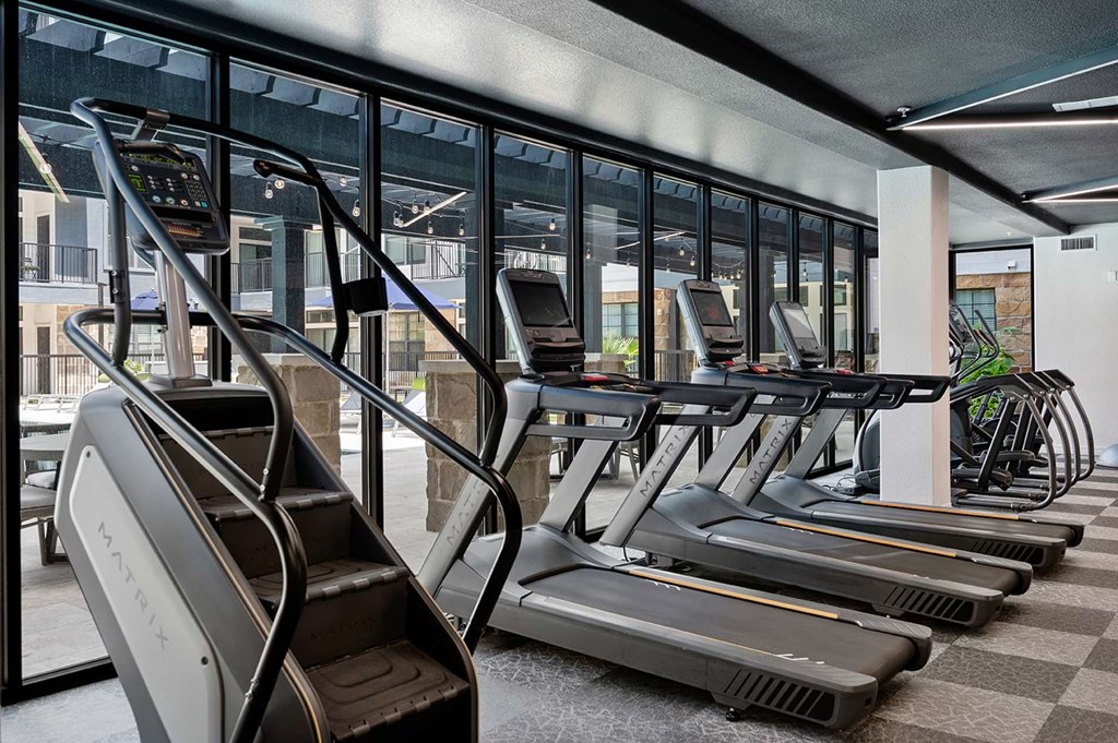Modern gym here at The Reserve at Arboretum Apartment Homes with large windows showcasing five treadmills and a stair climber. The setting is bright, clean, and inviting, suggesting an active atmosphere.