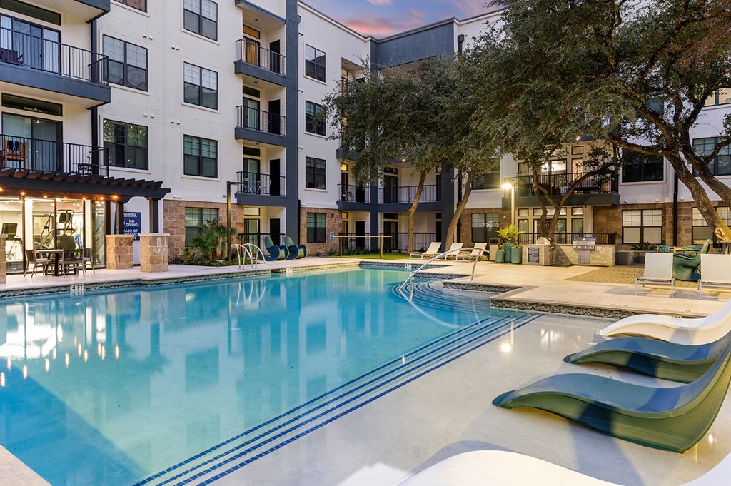 Modern courtyard here at The Reserve at Arboretum Apartment Homes with a serene outdoor pool area at dusk. Poolside loungers, soft lighting, and trees create a relaxing, inviting atmosphere.