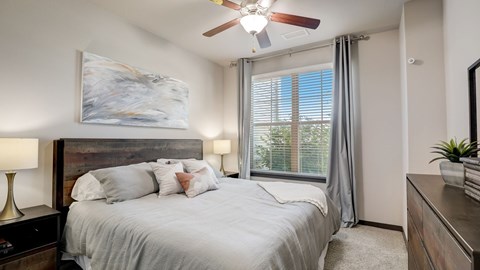 A bedroom with a large bed, a ceiling fan, and a painting on the wall.