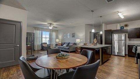A modern open-concept kitchen, dining, and living room with a wooden dining table and chairs.