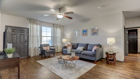 A living room with a grey couch, a wooden table, and a ceiling fan.