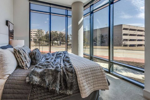 A bedroom with a large bed and a view of a parking lot through the windows.