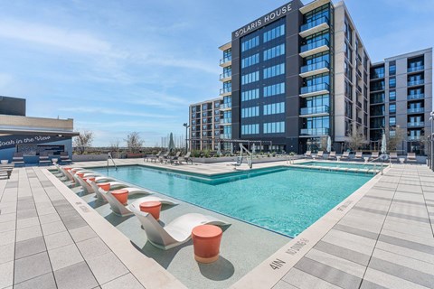 A large swimming pool with orange chairs in front of a Solaris House building.