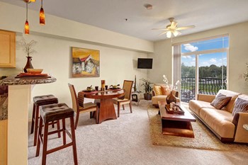 A living room with a ceiling fan and large windows overlooking the property Park Plaza II Living Room - Photo Gallery 5