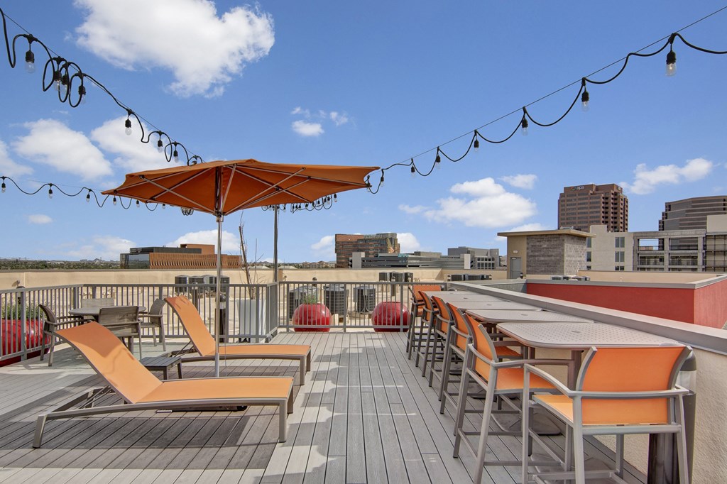 a rooftop deck with orange lounge chairs and umbrellas
