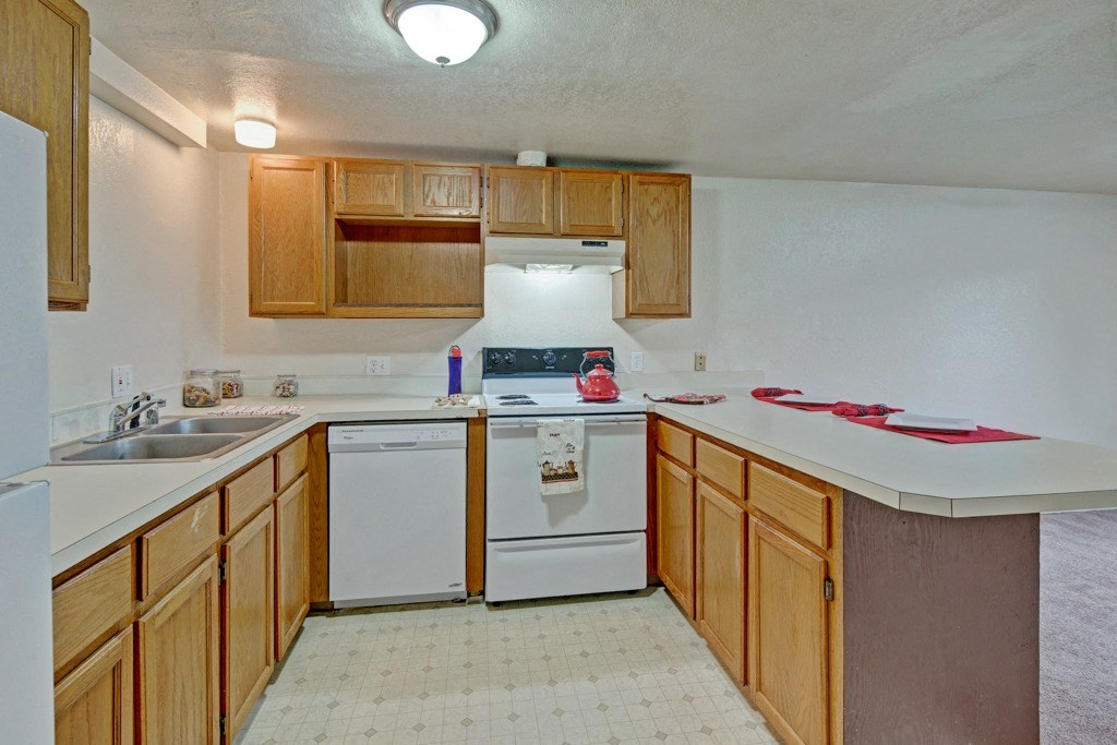 Spacious kitchen here at Ptarmigan Meadows with wooden cabinets, white countertops, and appliances. A red kettle on the stove, and a bright, welcoming atmosphere.