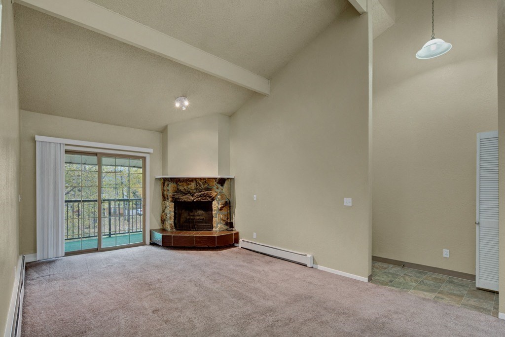 Spacious living room here at Ptarmigan Meadows with high ceilings, featuring a stone fireplace and large sliding glass doors to a balcony. Neutral tones create a calm atmosphere.