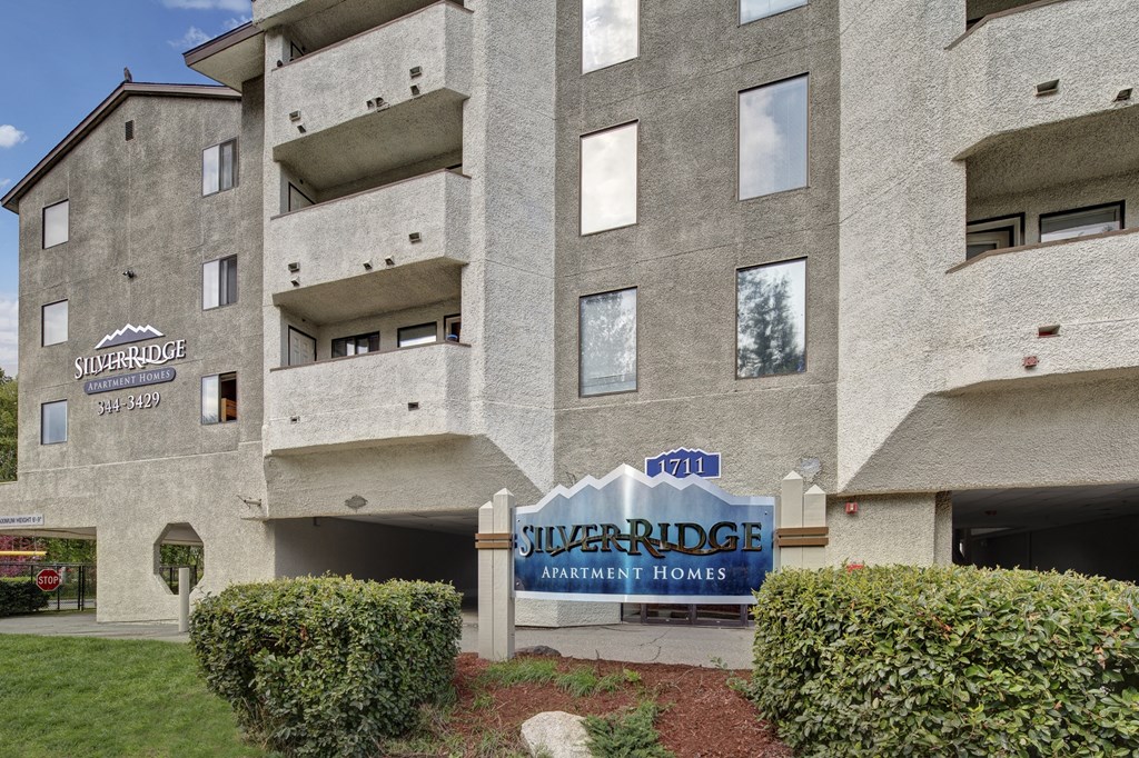Exterior of Silver Ridge Apartment Homes, featuring textured gray walls, multiple balconies, and a prominent blue sign with the address number 1711.