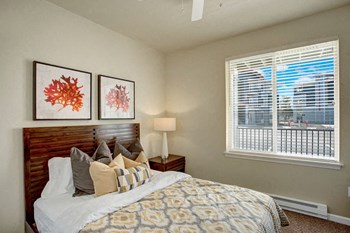 A bedroom with a large window looking out to the patio and the rest of the property with a bed, nightstand, and ceiling fan Solara Bedroom - Photo Gallery 5
