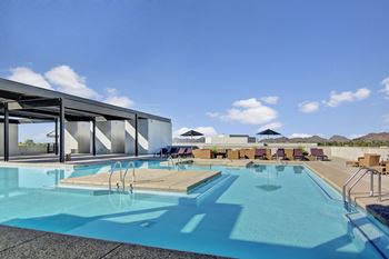 a large swimming pool with lounge chairs and umbrellas on a sunny day