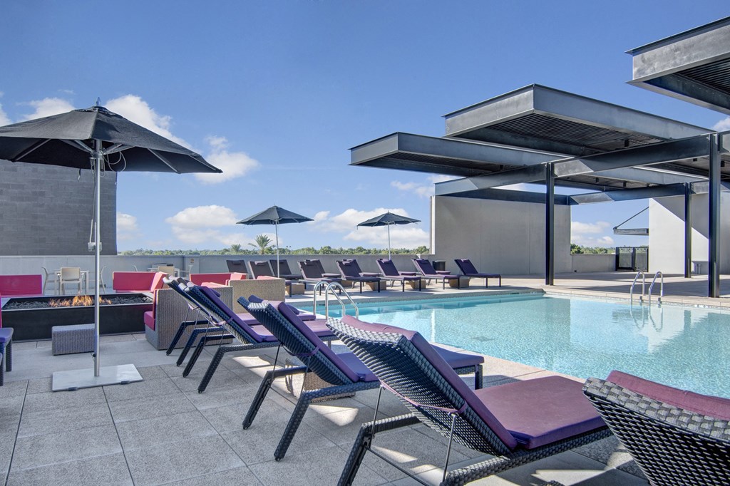 Rooftop pool here at Trend at 51 Apartments with modern loungers and black umbrellas under a clear blue sky. The scene conveys relaxation and leisure with a luxurious ambiance.