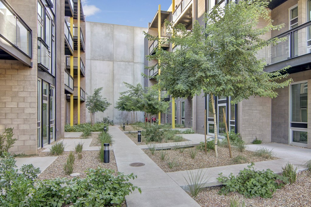 Modern courtyard here at Trend at 51 Apartments with a serene atmosphere in an apartment complex. Features concrete paths, greenery, and small trees next to a multi-story building.