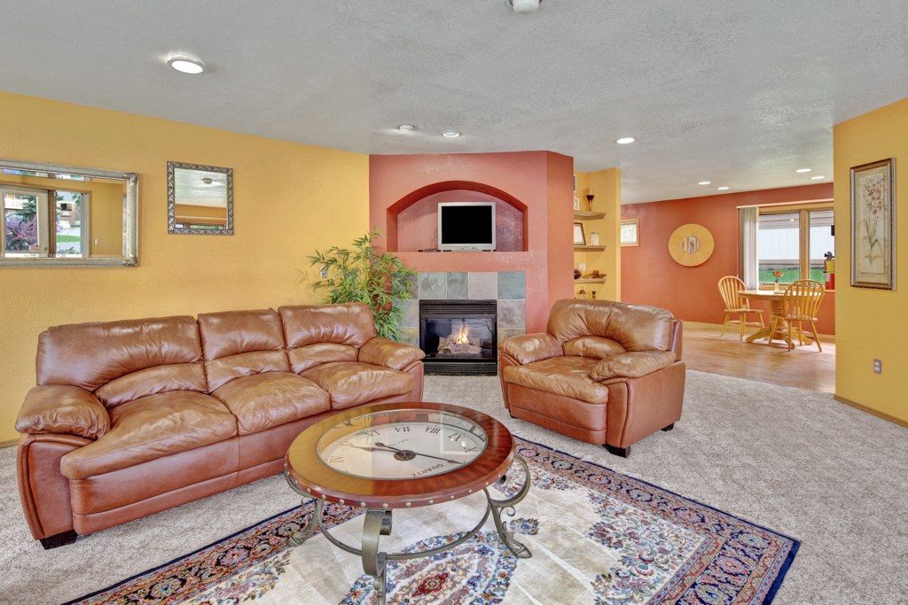 Warm living room here at Wildwood Estates Apartments with yellow and red walls, featuring leather sofas, a glass coffee table, fireplace, and a dining area with wooden chairs in the background.