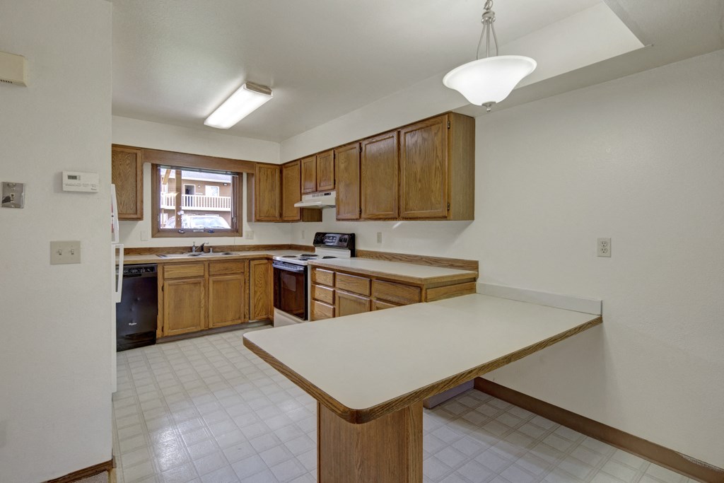 Spacious kitchen here at Wildwood Estates Apartments with wooden cabinets, white countertops, and an island. Bright natural light from window, creating an inviting and clean atmosphere.