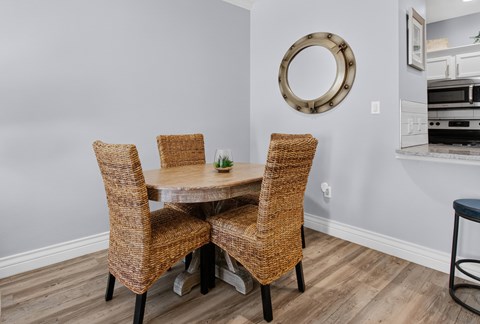 A dining room with a round mirror and a table with four chairs.