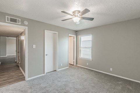 an empty living room with a ceiling fan and a hallway