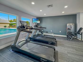 A Spin bike is in a room with a view of a pool and a house.